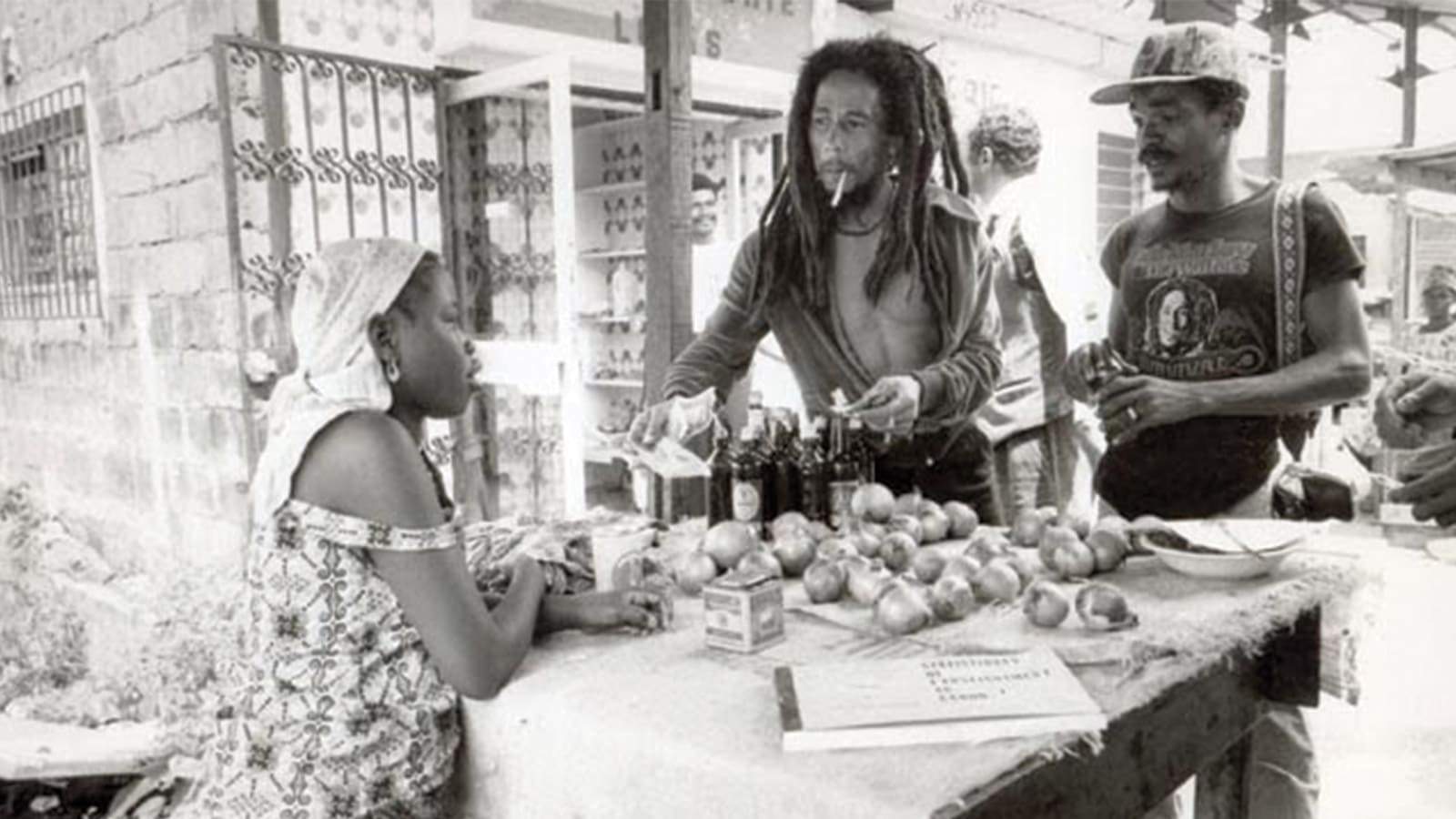 Bob Marley accompagné d'un ami, faisant ses courses au marché, discutant avec une femme commerçante