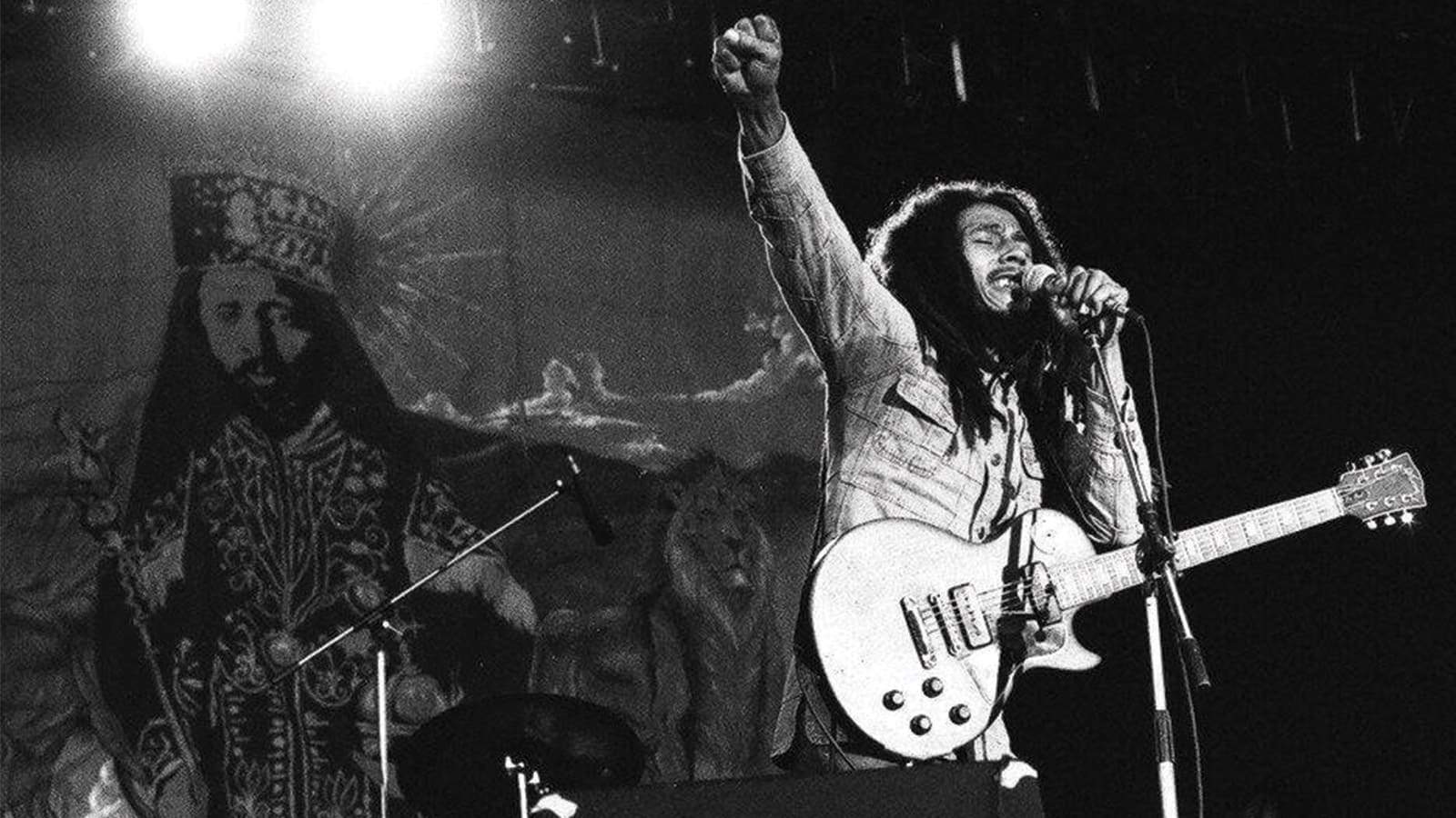 Bob marley en concert reggae avec sa guitare, le poing levé au ciel