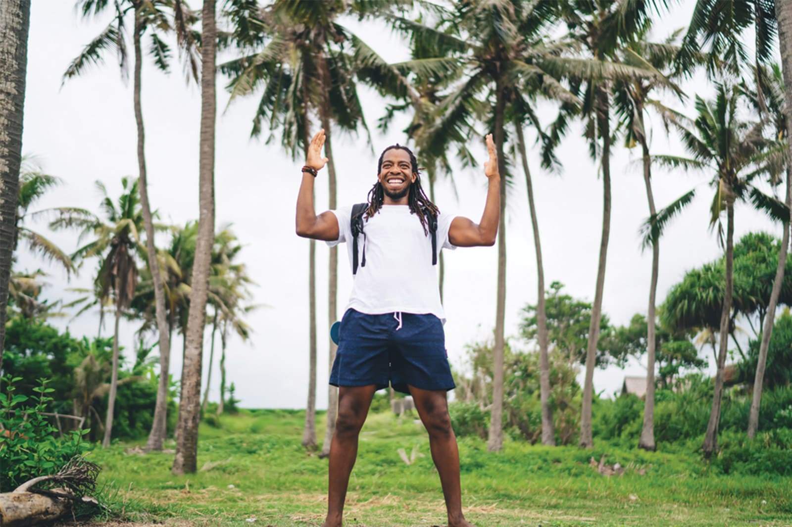 Homme noir avec Dreadlocks se tenant debout entre des palmiers, super heureux et en forme