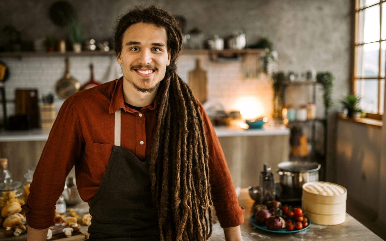 Cuisinier avec dreadlocks souriant assis sur sa table