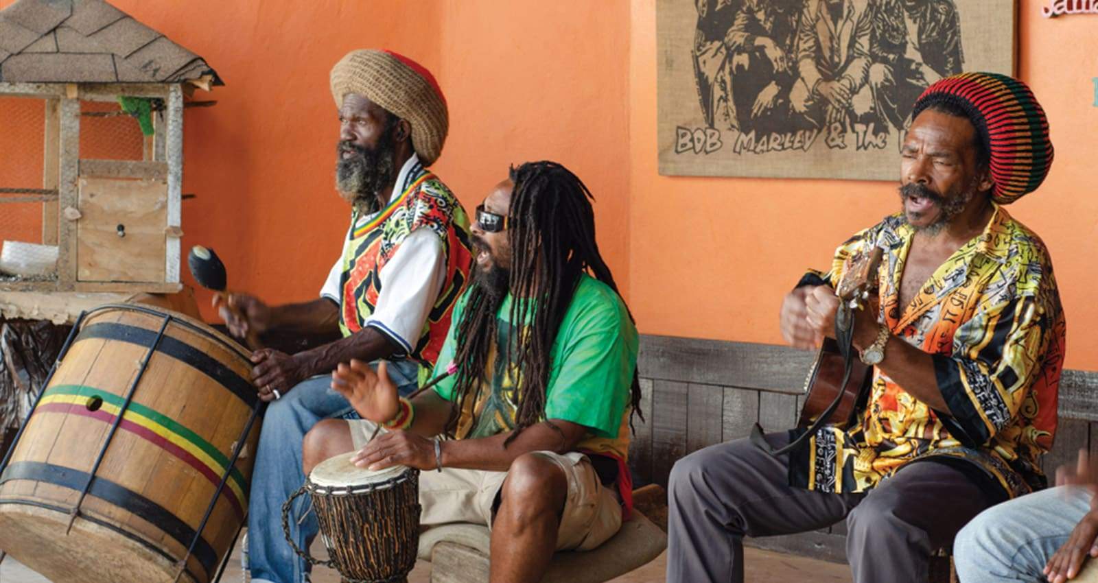 trois-jamaicains-jouant-du-reggae-sur-une-scene,-avec-un-poster-de-bob-marley-and-the-wailers-accroché-au-mur